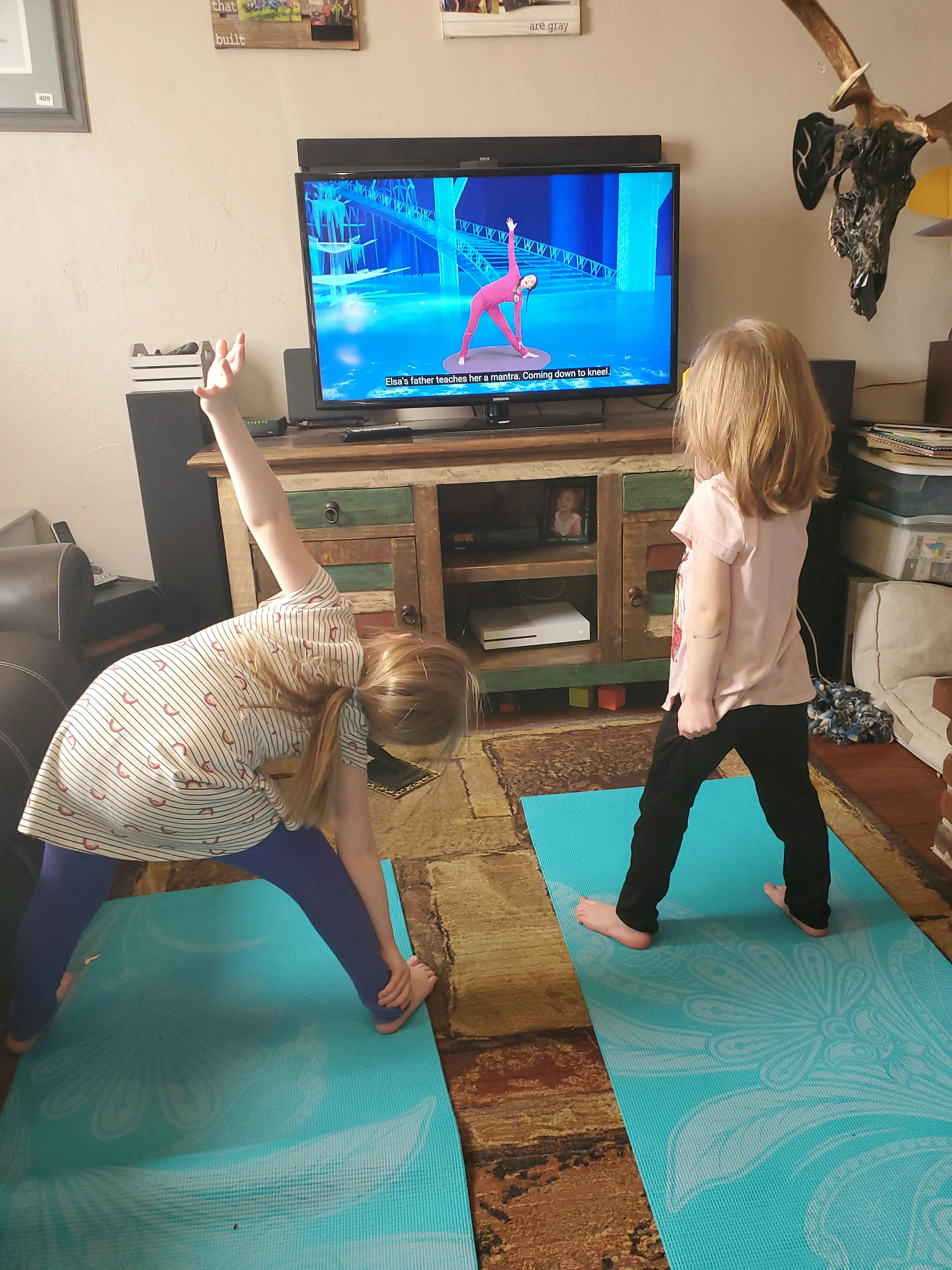 Person and child doing yoga poses on mats in front of a TV