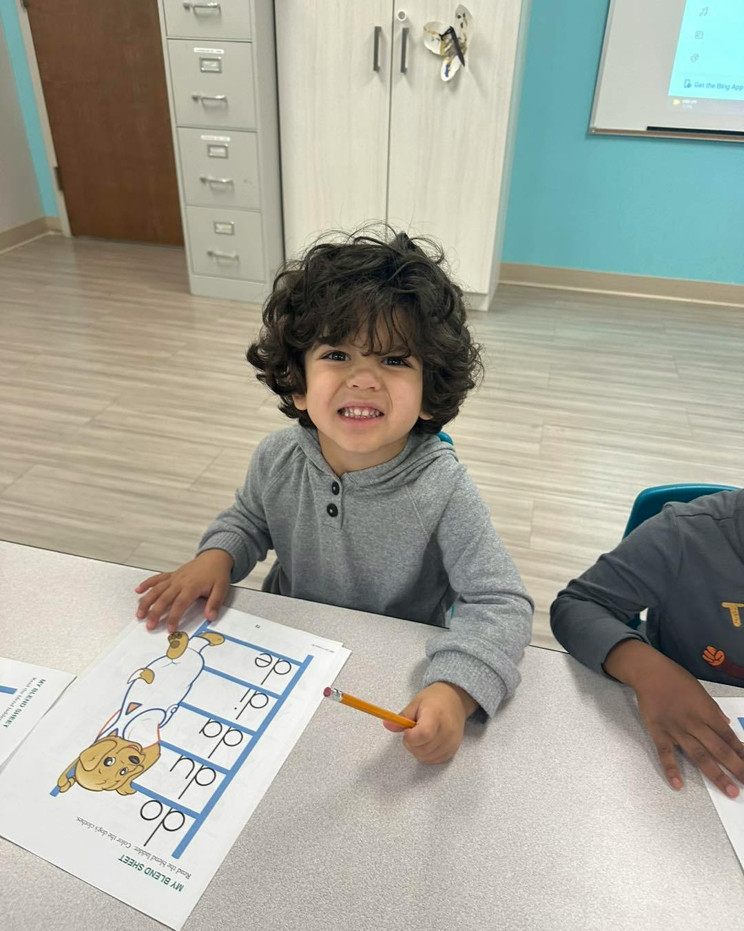 Child with curly hair holding a pencil and looking at a worksheet