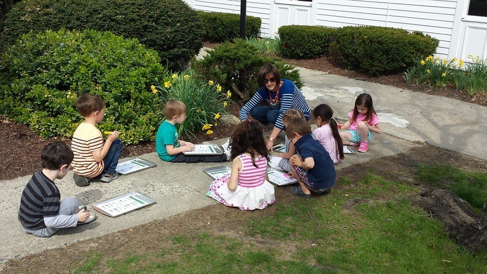 Adult and children sitting on ground with papers outdoors