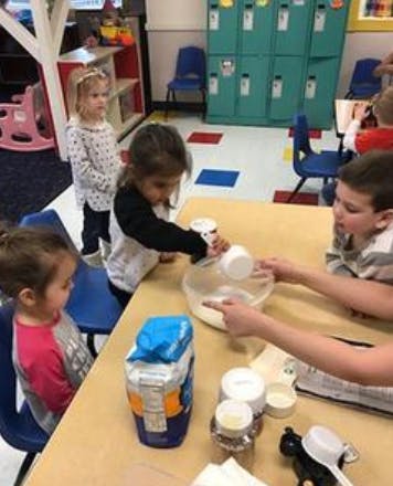 Children at a table pouring ingredients into a bowl in a classroom