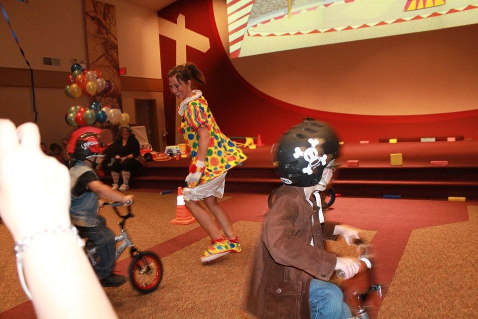Person in clown costume with two children on riding toys
