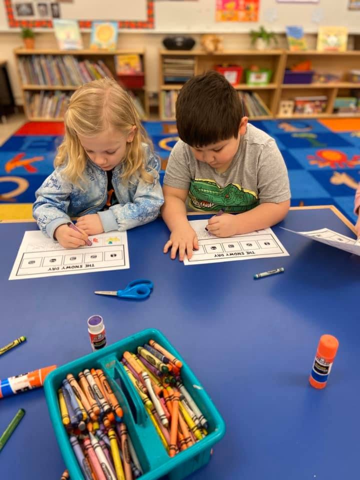 Two children coloring at a blue table in a classroom