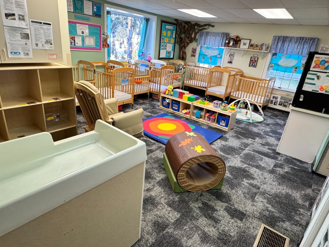 A classroom with several cribs, a changing table, and a play area