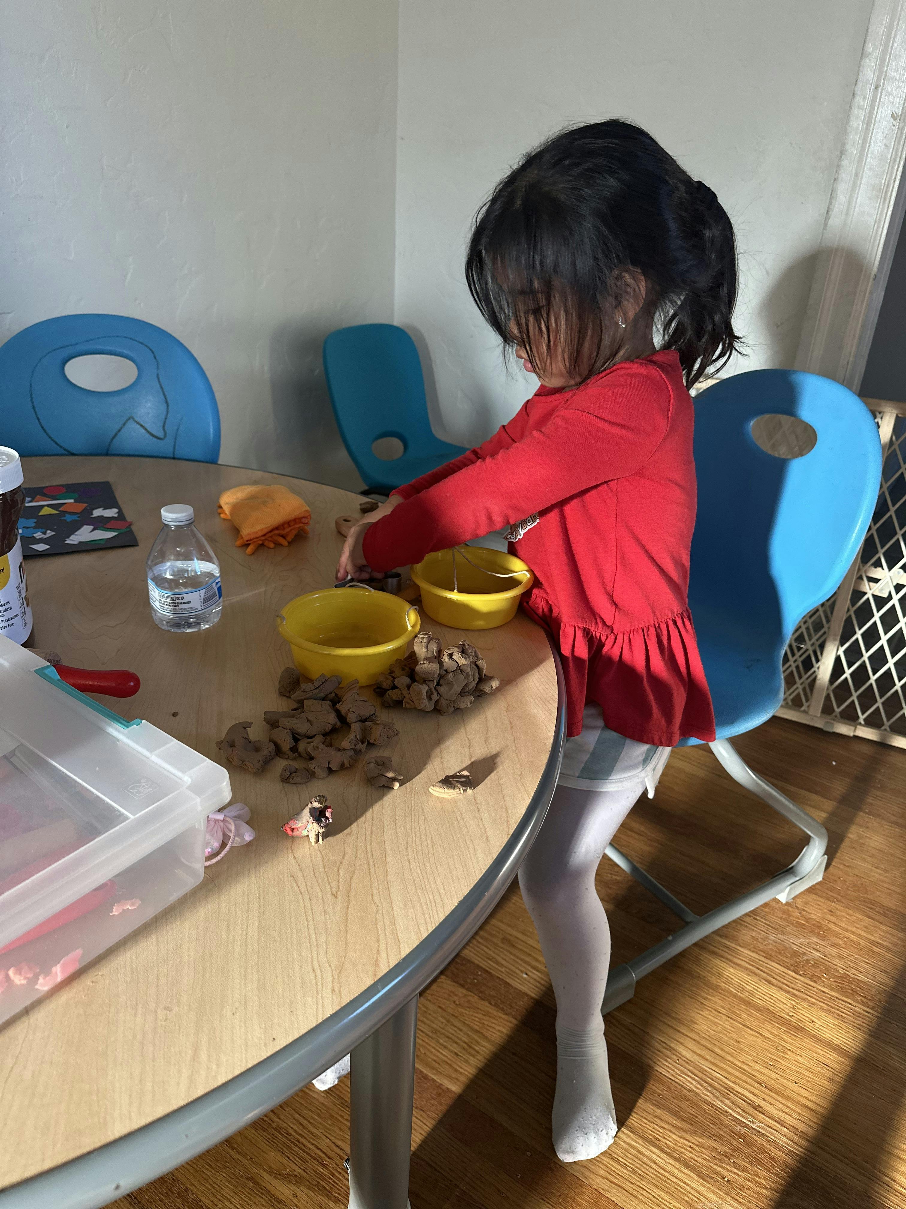 Child playing with clay and small yellow buckets on a round wooden table