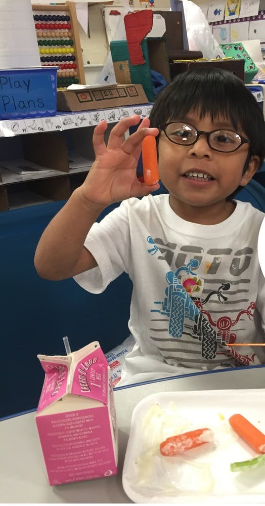 Child in glasses holding up a carrot stick