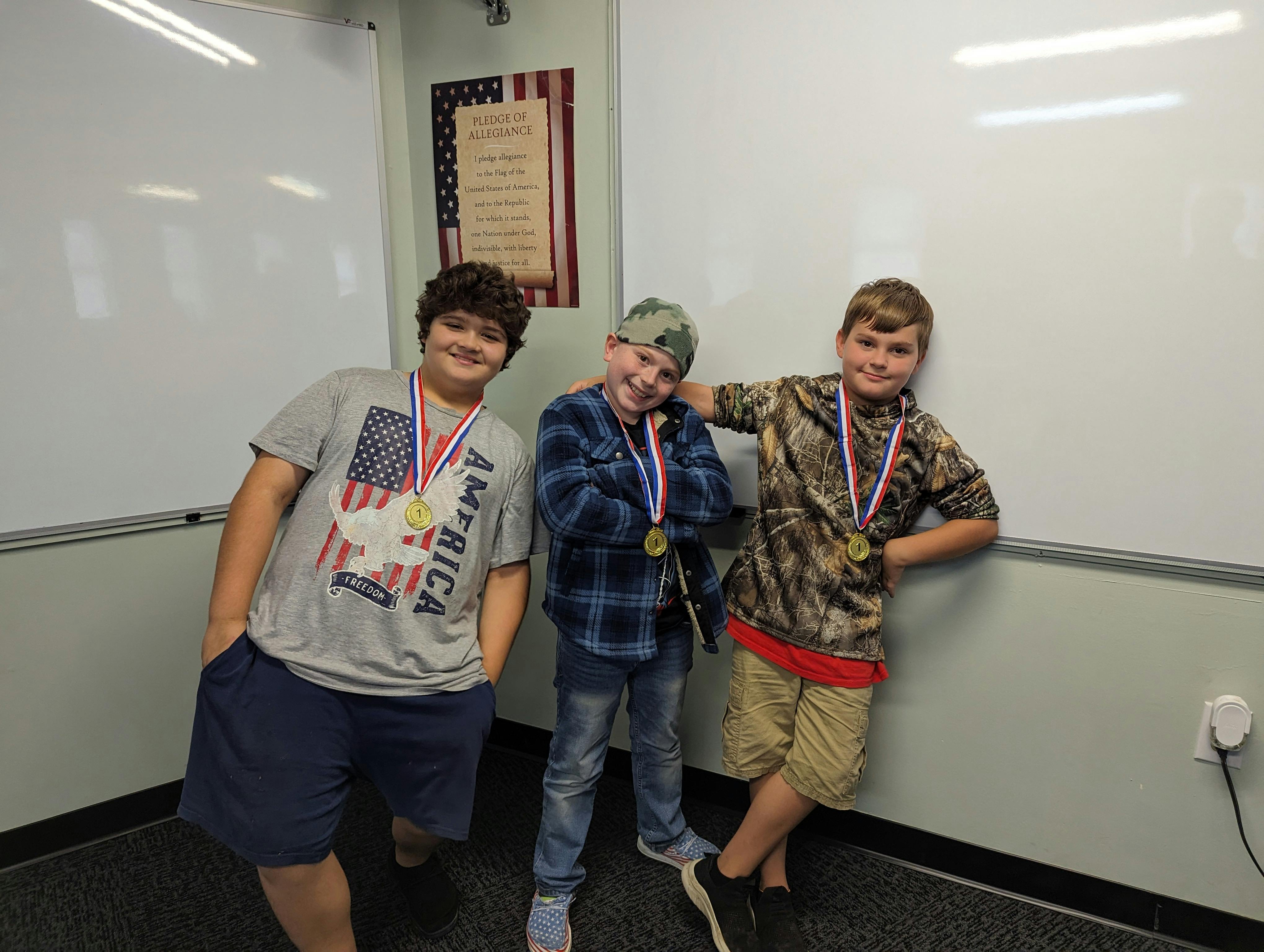 Three children wearing gold medals with '1' and red, white, and blue ribbons
