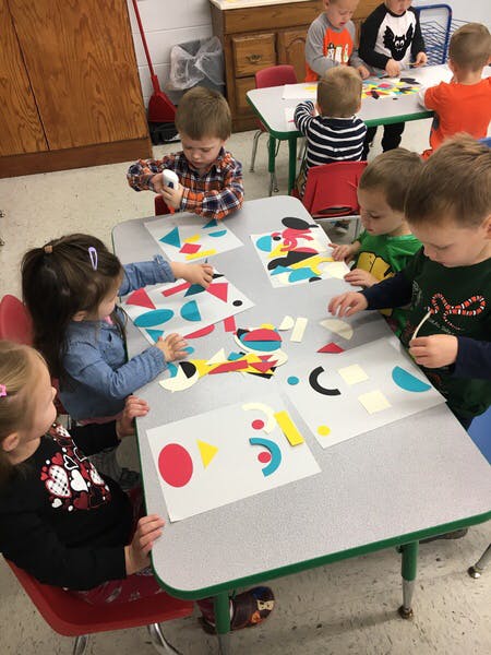 Children sitting at tables doing crafts with paper shapes
