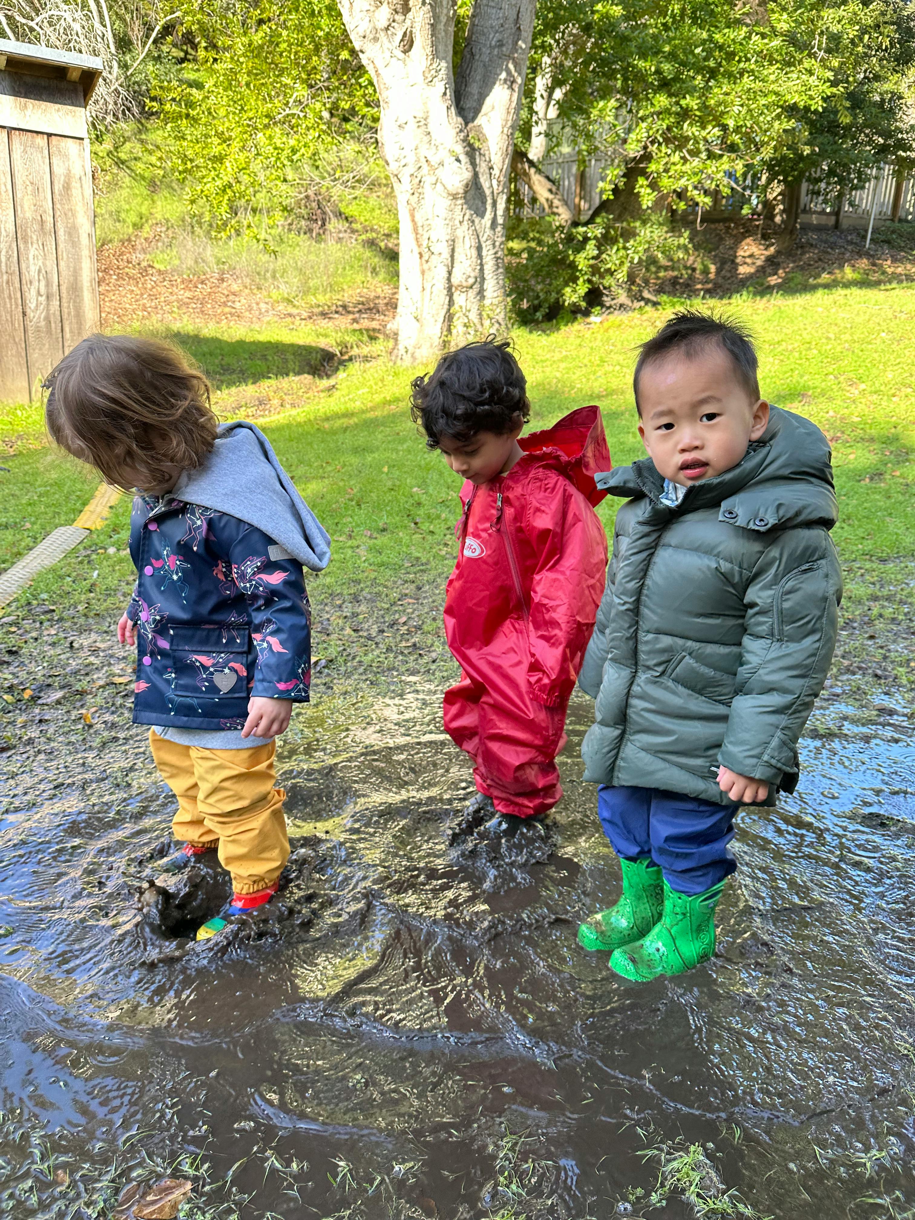 Three children standing in a muddy puddle