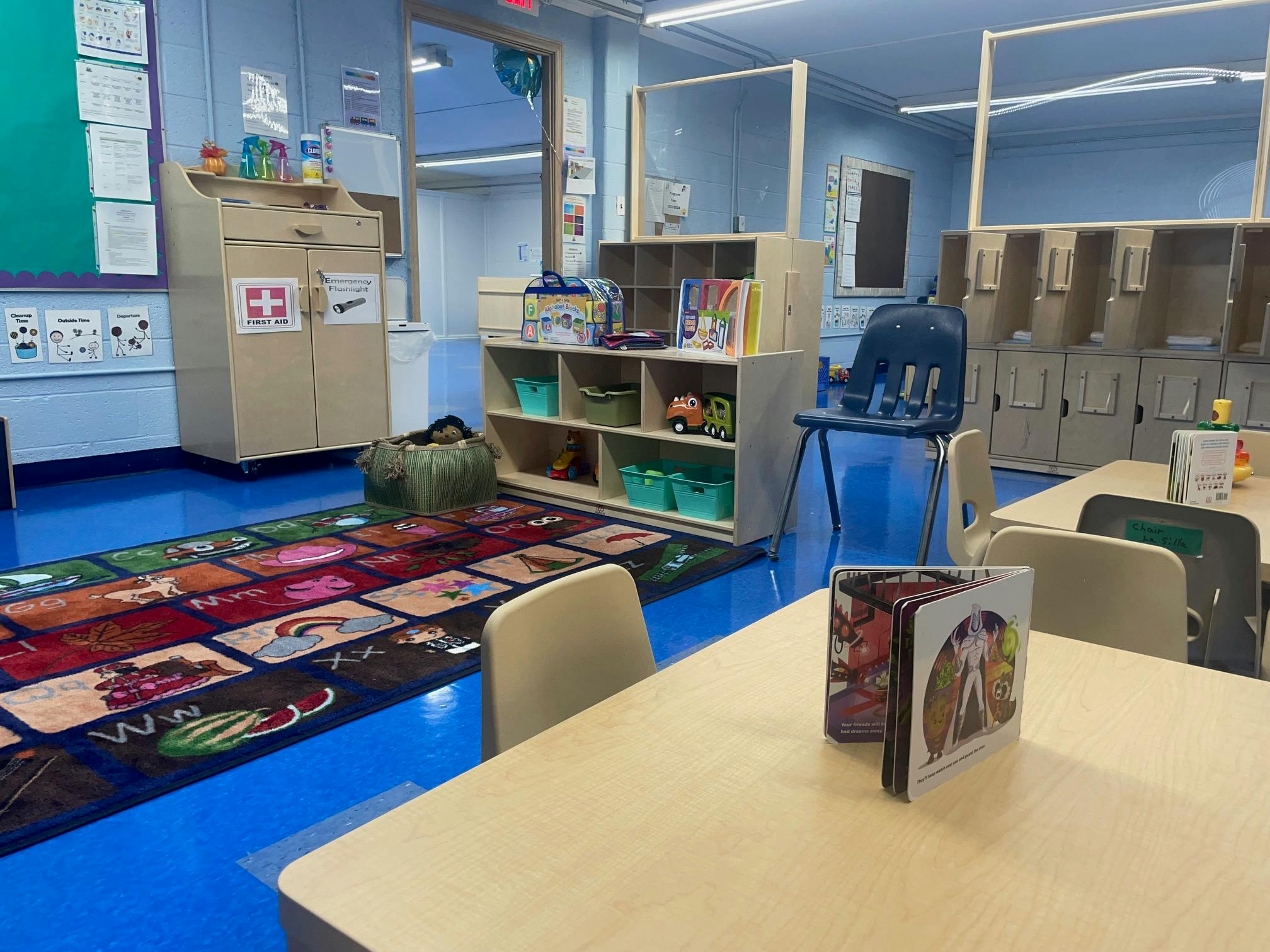 Classroom with small tables and chairs, a colorful rug, and storage shelves
