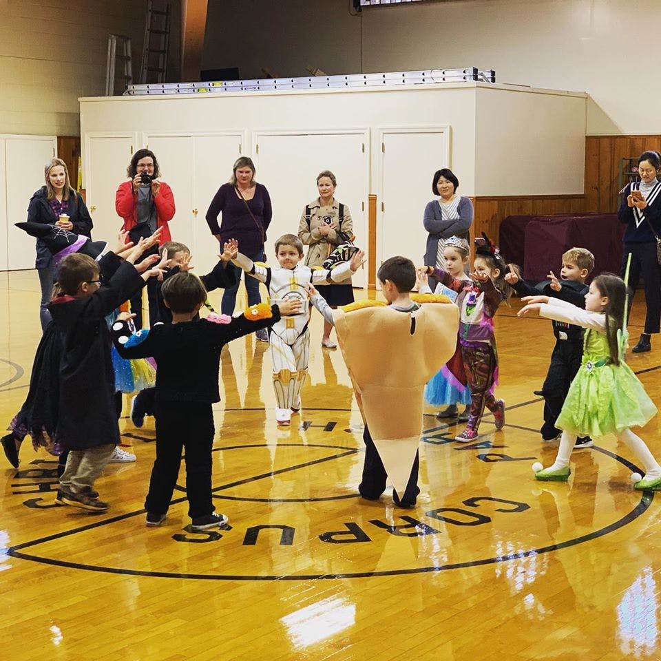 Children in costumes playing in a gymnasium with adults watching in the background