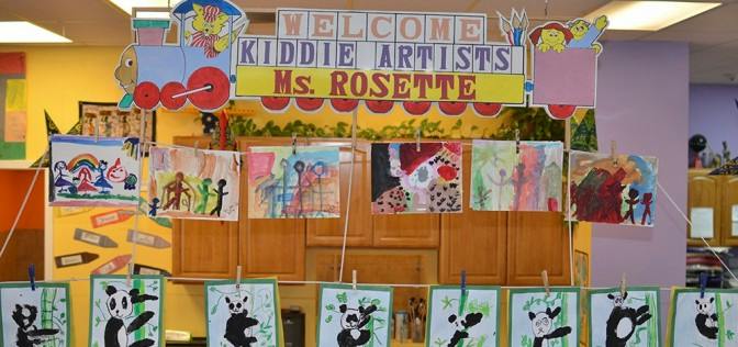 Children's artwork displayed in a classroom with a "Welcome Kiddie Artists" sign