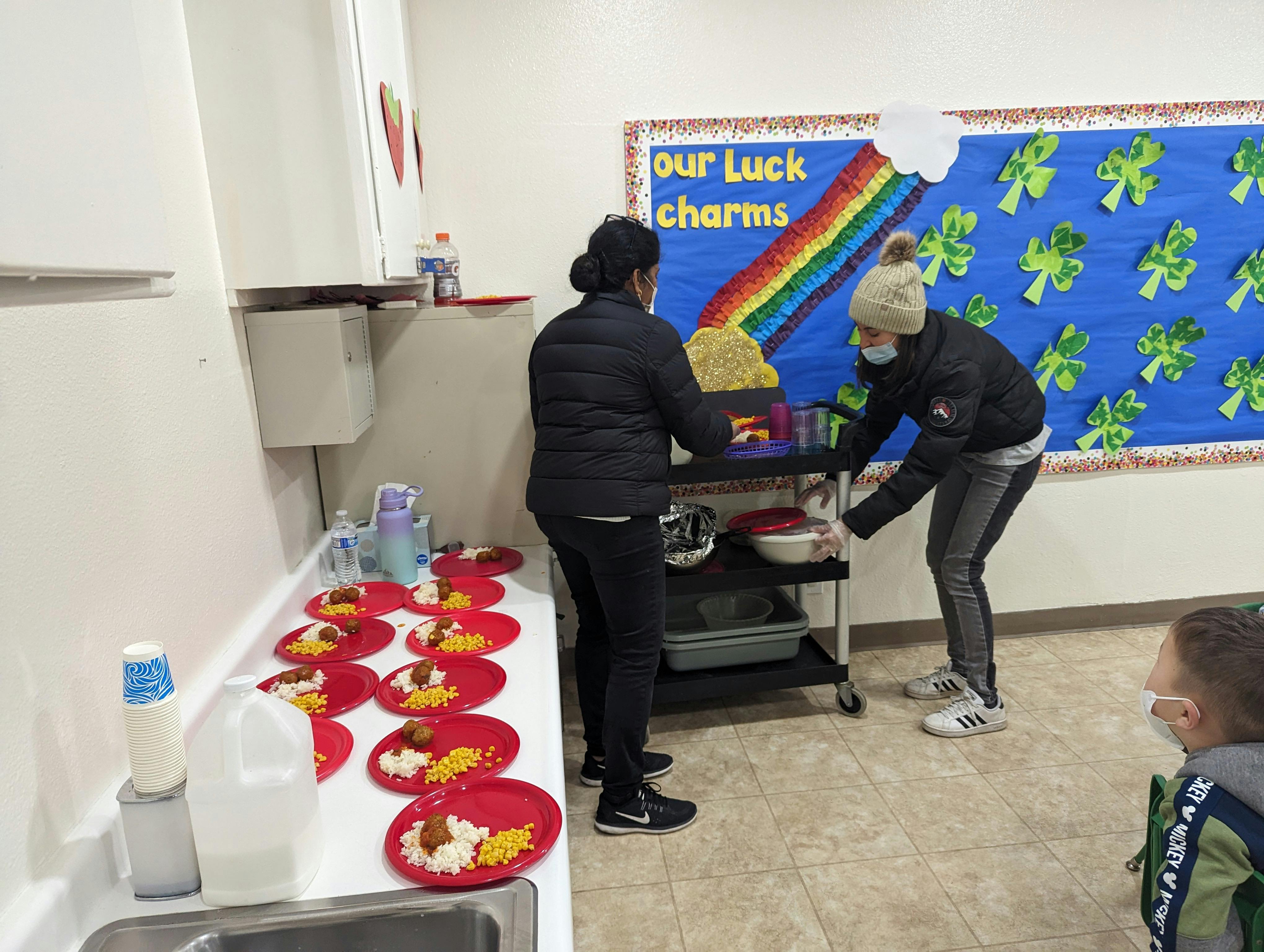 Two people serving food onto plates in a classroom