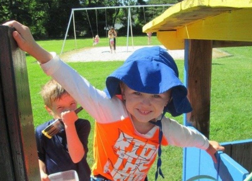 Child in blue hat on playground structure with another child behind