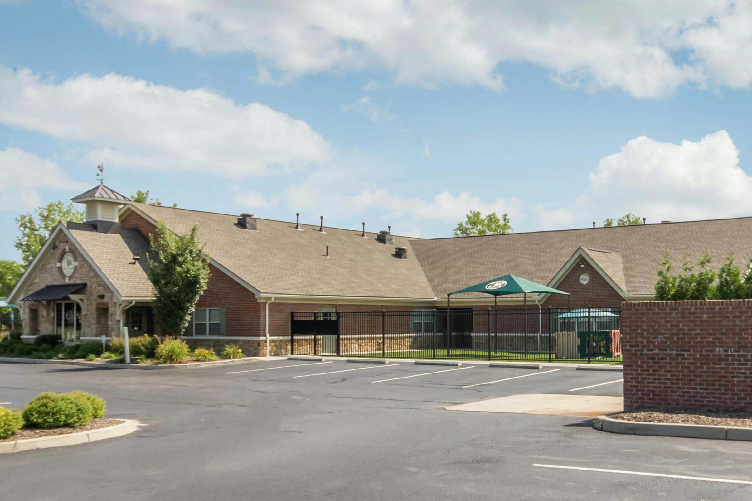 Brick building with a parking lot in front and a fenced-in playground area
