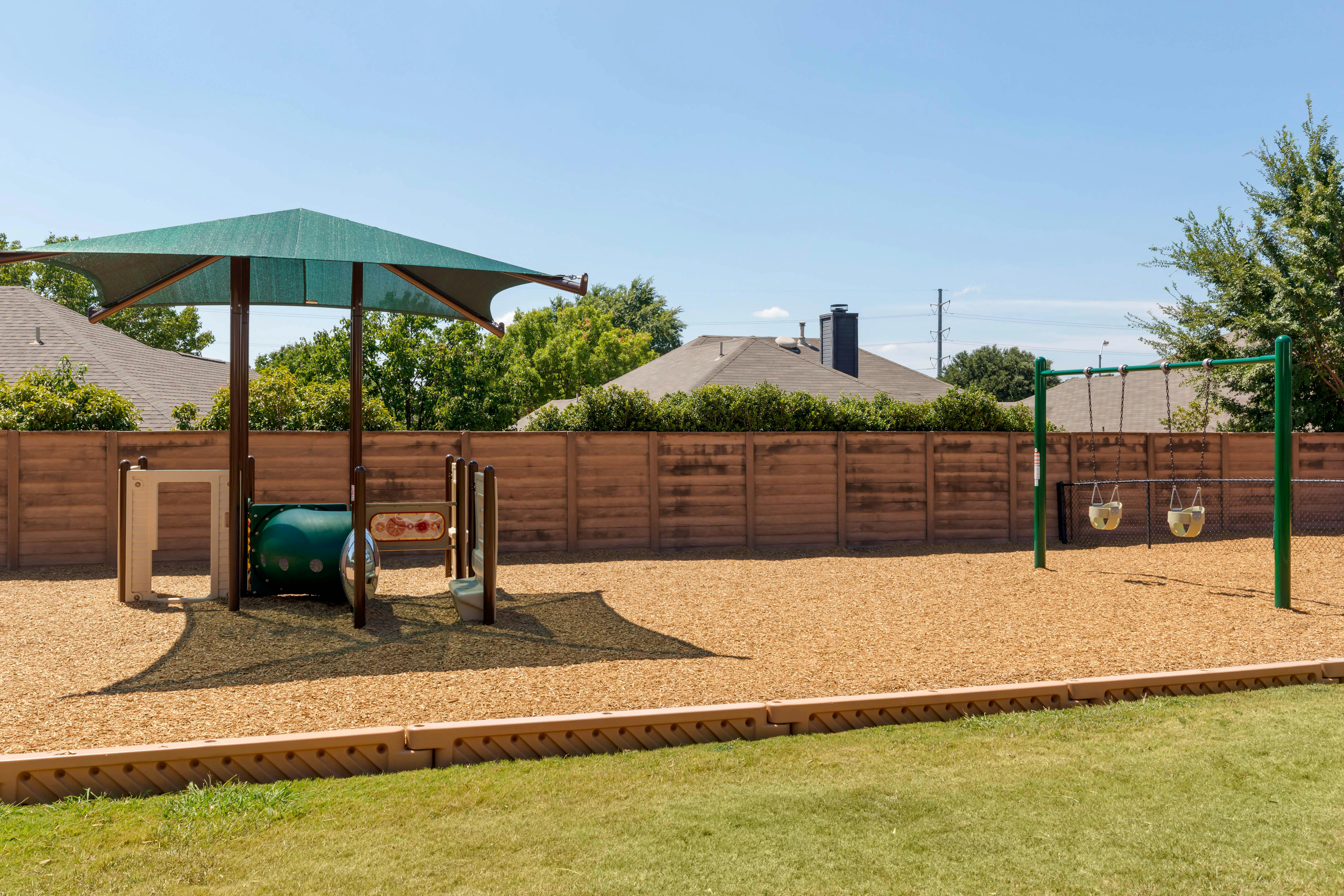 Playground with swings, a tunnel, and a green canopy over wood chips