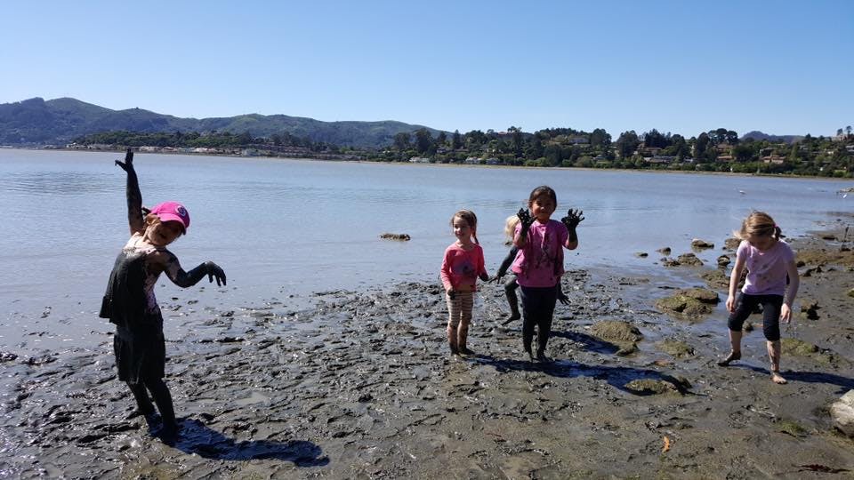 Children playing in mud on a beach next to water