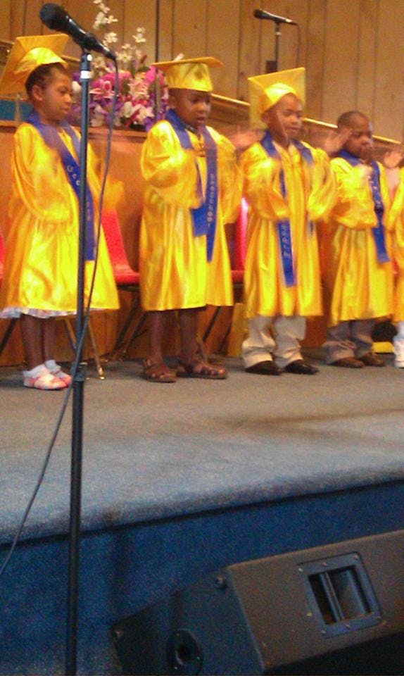 Children in yellow graduation gowns and caps standing on a stage
