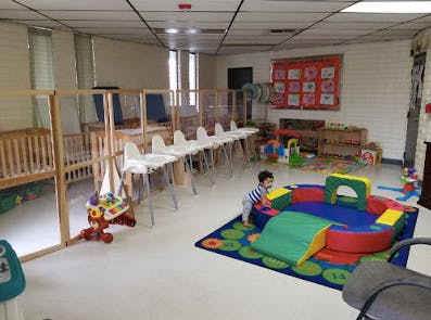 Child playing in a daycare room with cribs and high chairs