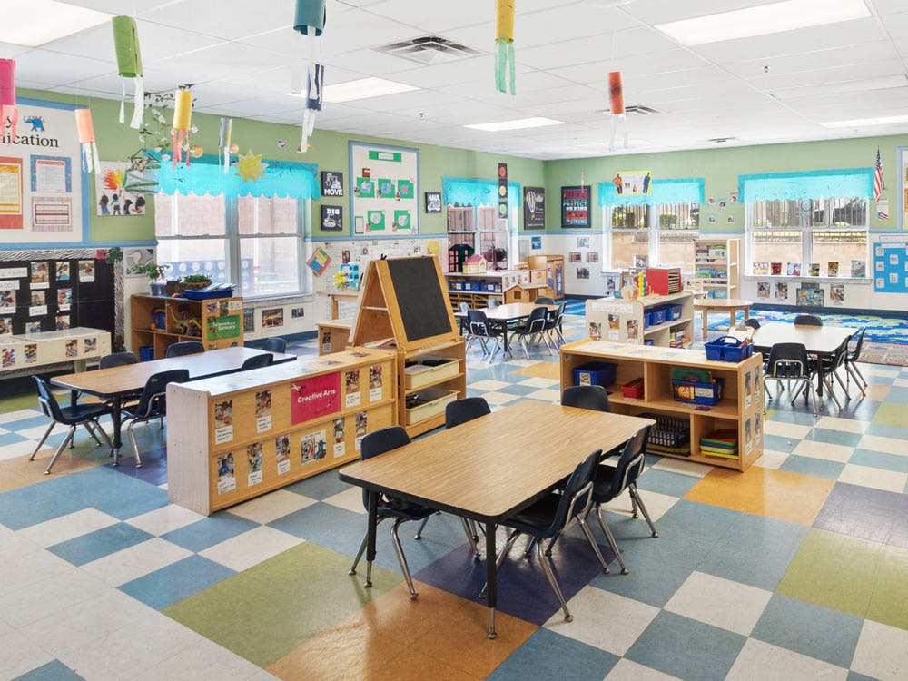 Empty classroom with small tables and chairs, shelves, and decorations
