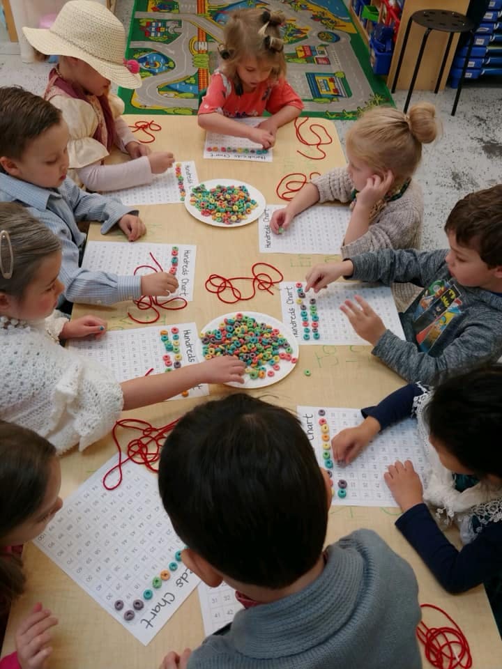 Children at a table with plates of colorful cereal and red yarn