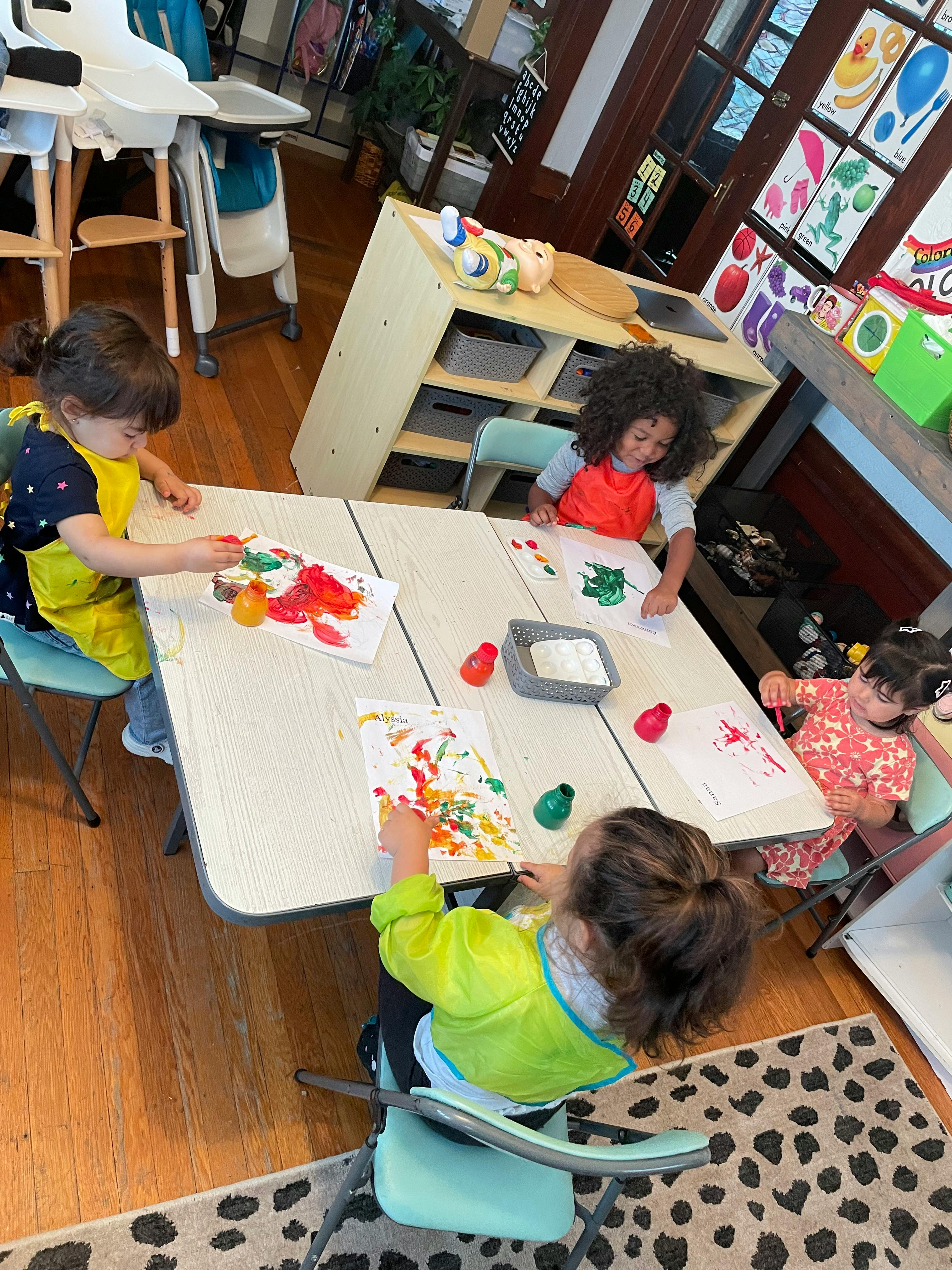Four children painting at a table in a classroom