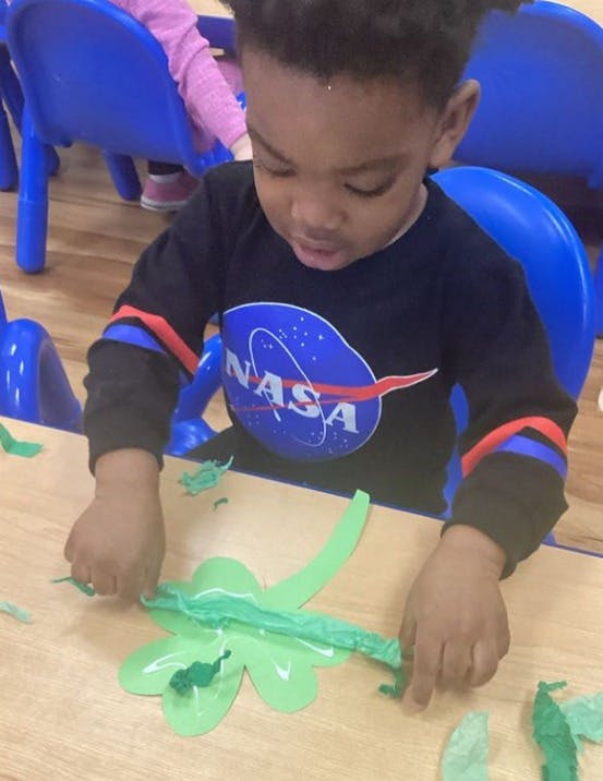 Child in a classroom working on a craft project with green paper
