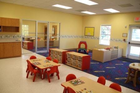 Empty classroom with small tables and chairs, storage units, and play equipment