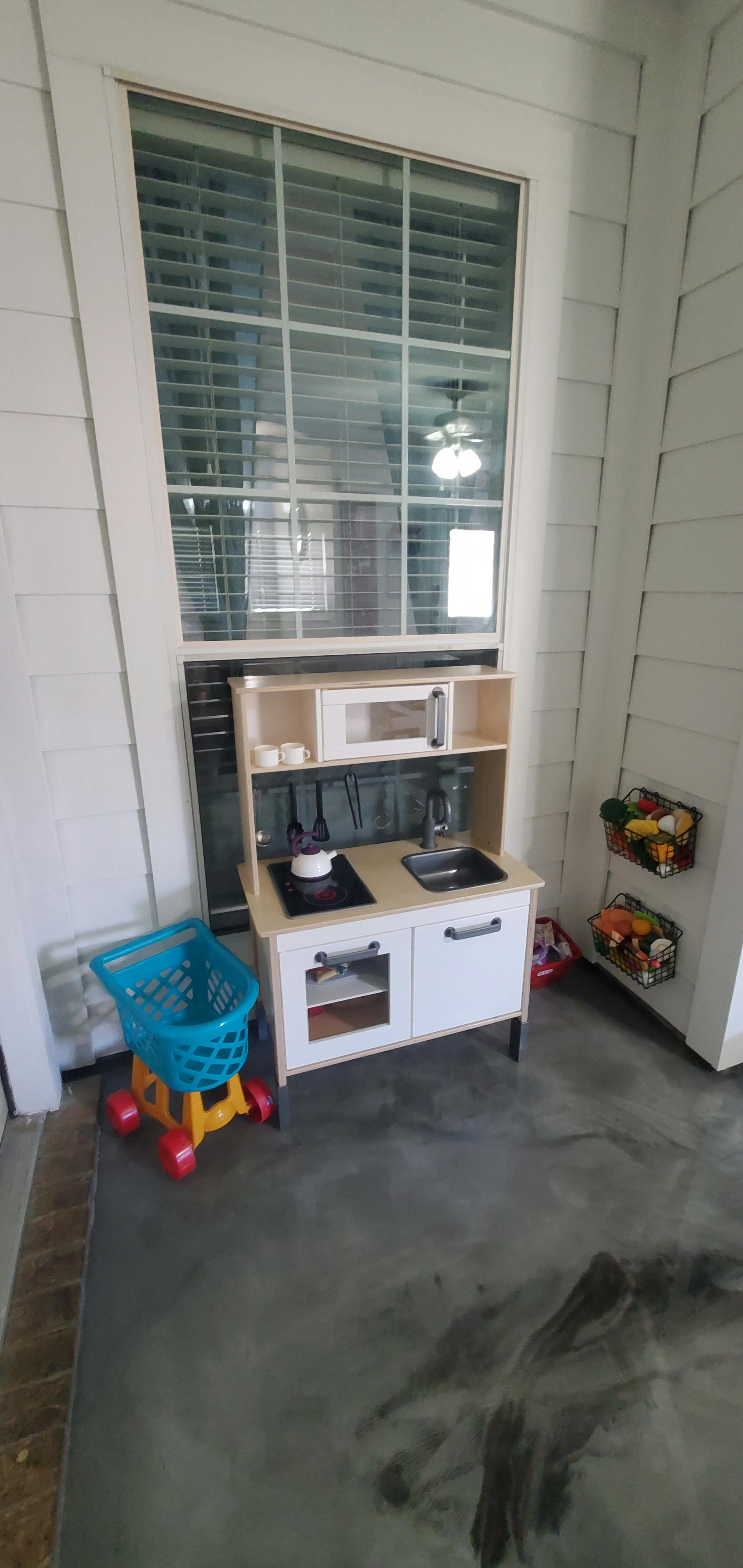 Toy kitchen set and shopping cart next to a large window