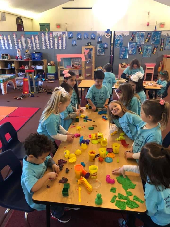 Children playing with modeling clay at a table in a classroom