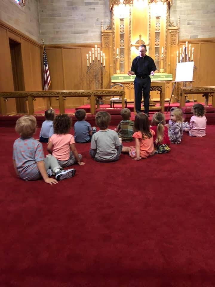 Adult speaking to a group of children sitting on a red carpet