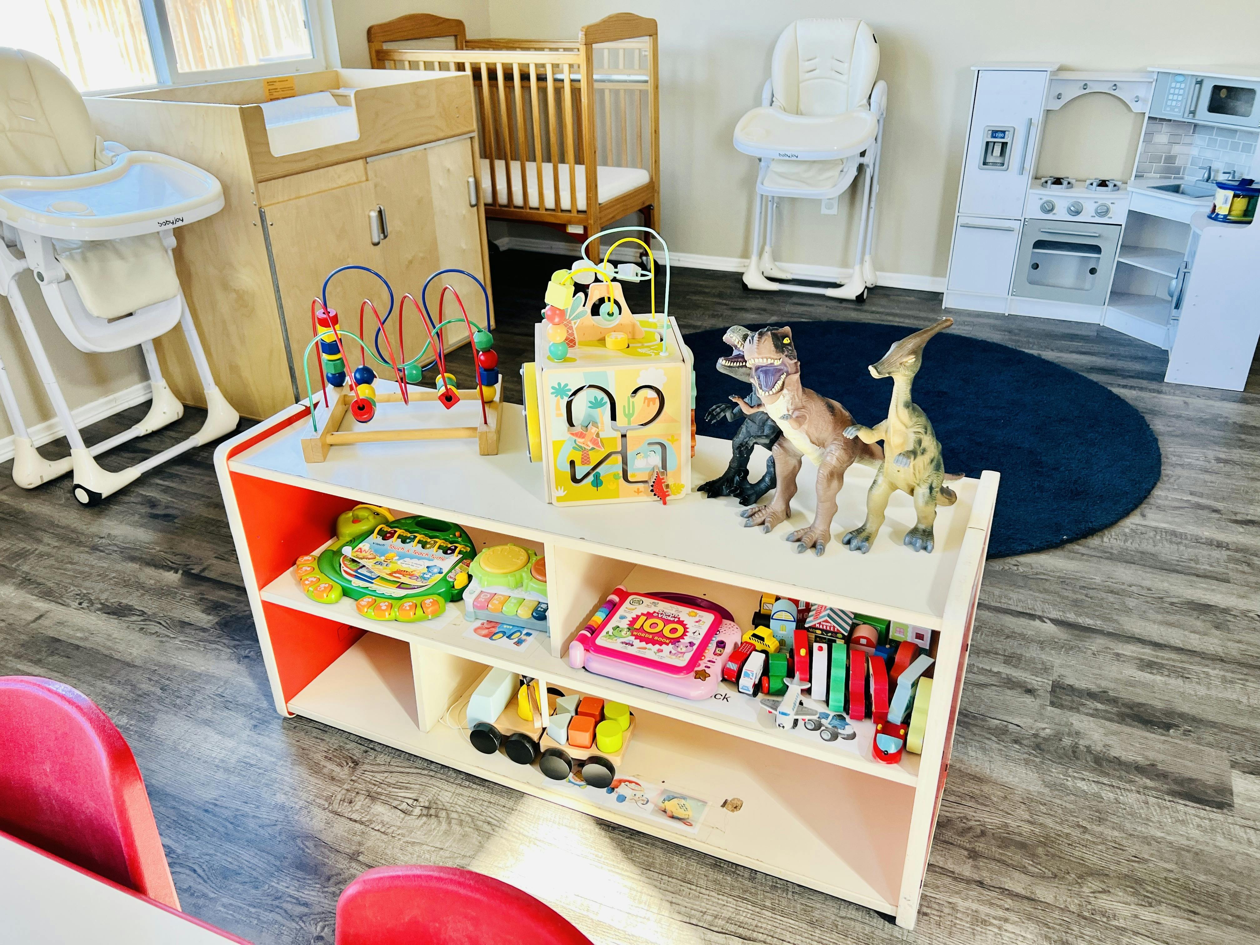 Children's room with a changing table, crib, high chairs, toy kitchen, and toy shelf