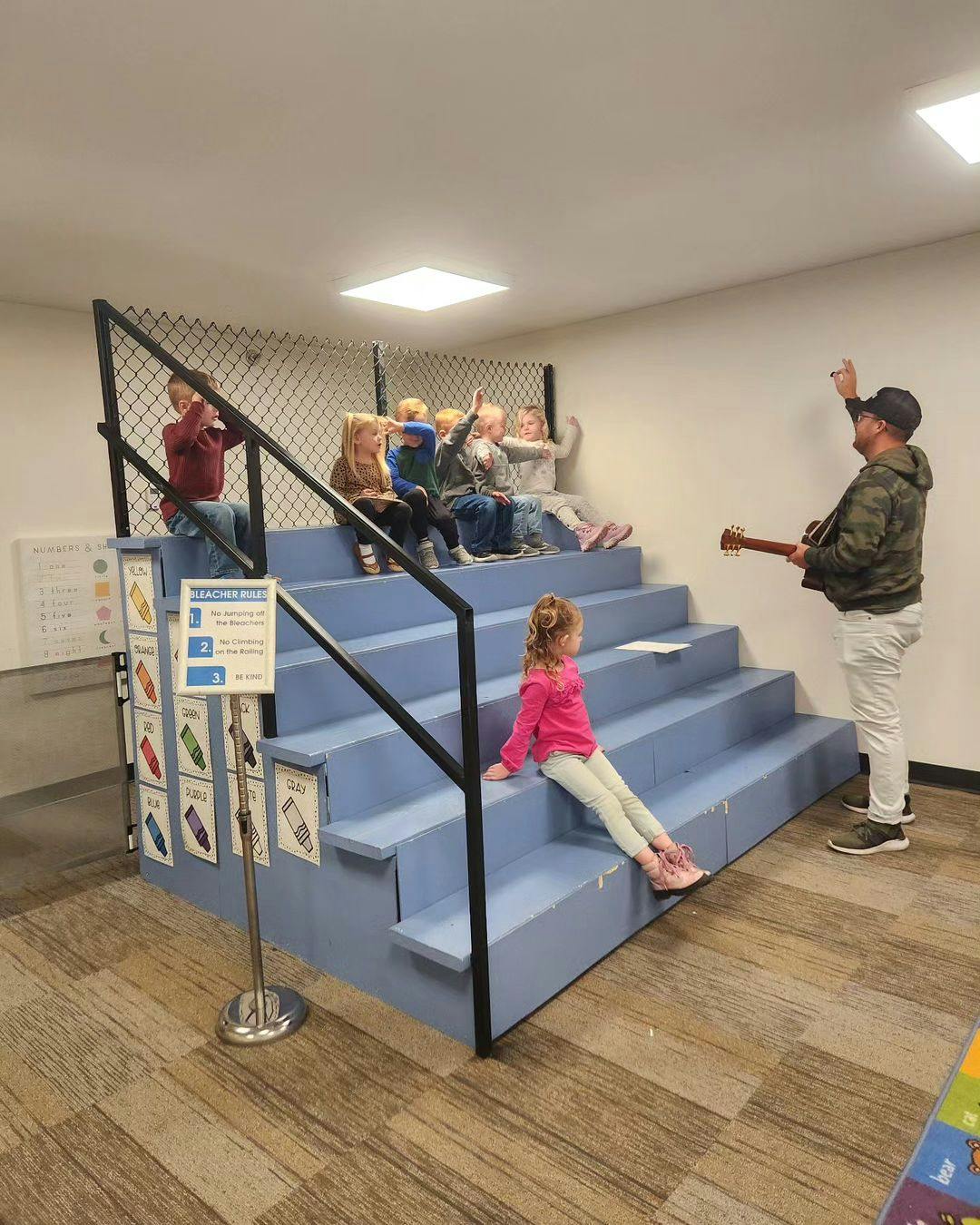 Person playing guitar for children sitting on steps