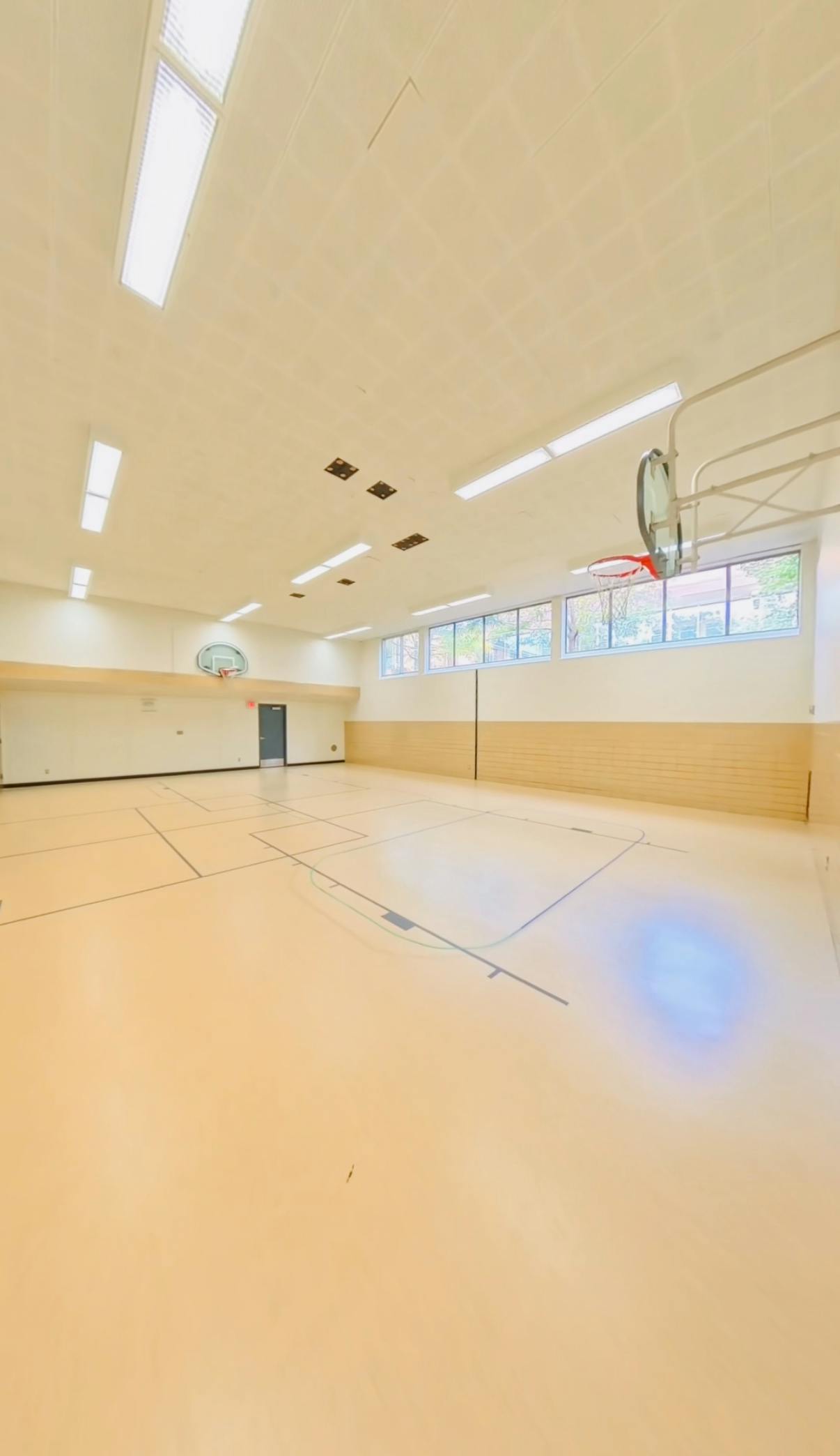 Empty gymnasium with basketball hoops on both ends and windows along one wall