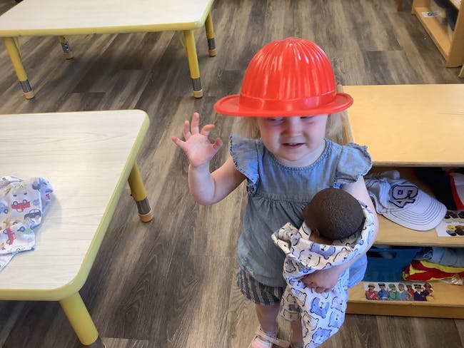 Child wearing a red hat and holding a doll, waving