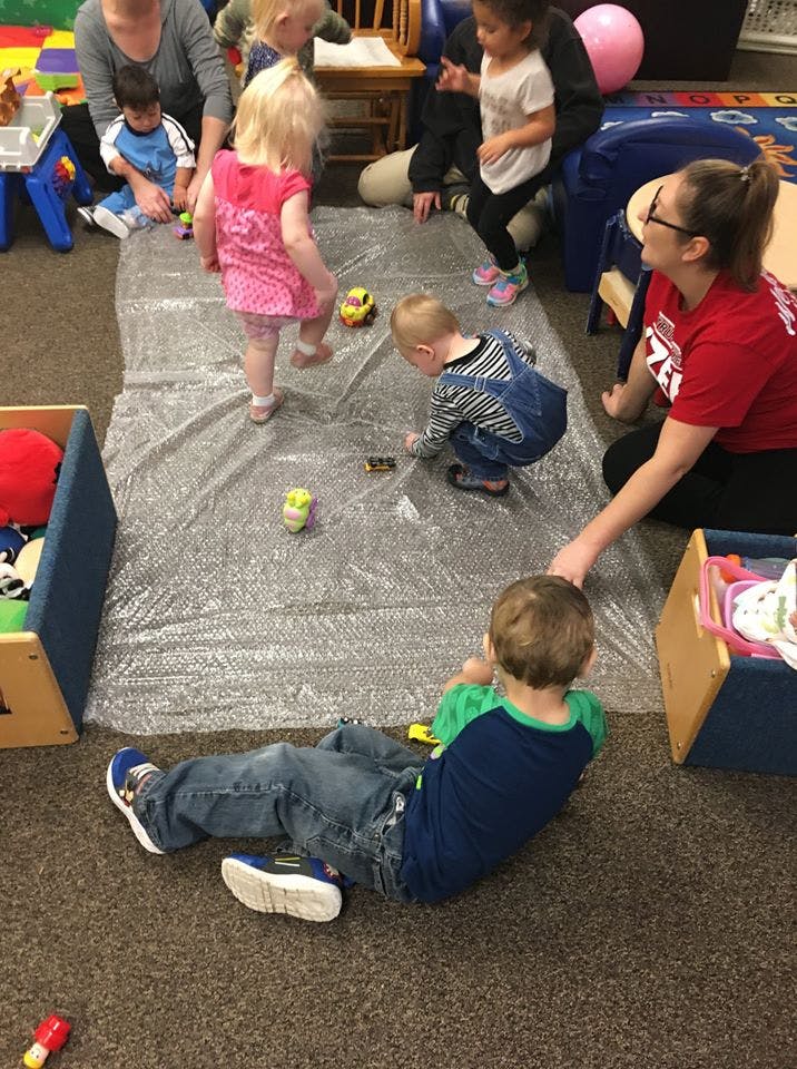 Adults and children playing with toys on a plastic sheet on the floor