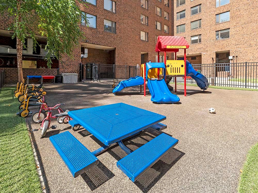 A playground with a blue picnic table, tricycles, and play structure with slides