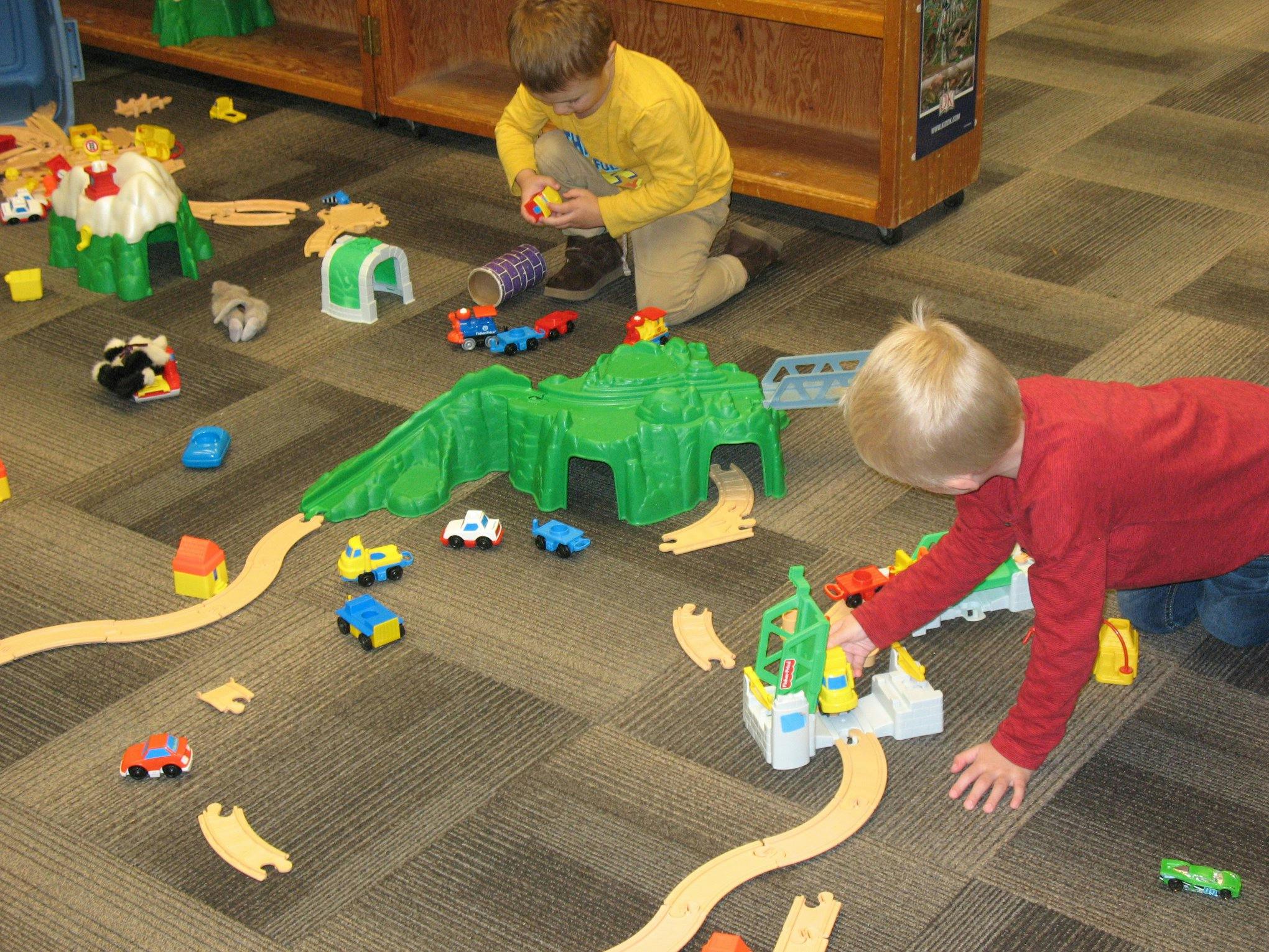 Two children playing with toy cars and train tracks on a carpeted floor