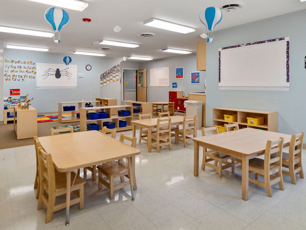 Classroom with small wooden tables and chairs, shelving units, and hot air balloon decorations