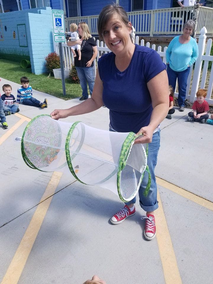 Person holding a butterfly habitat with children in the background