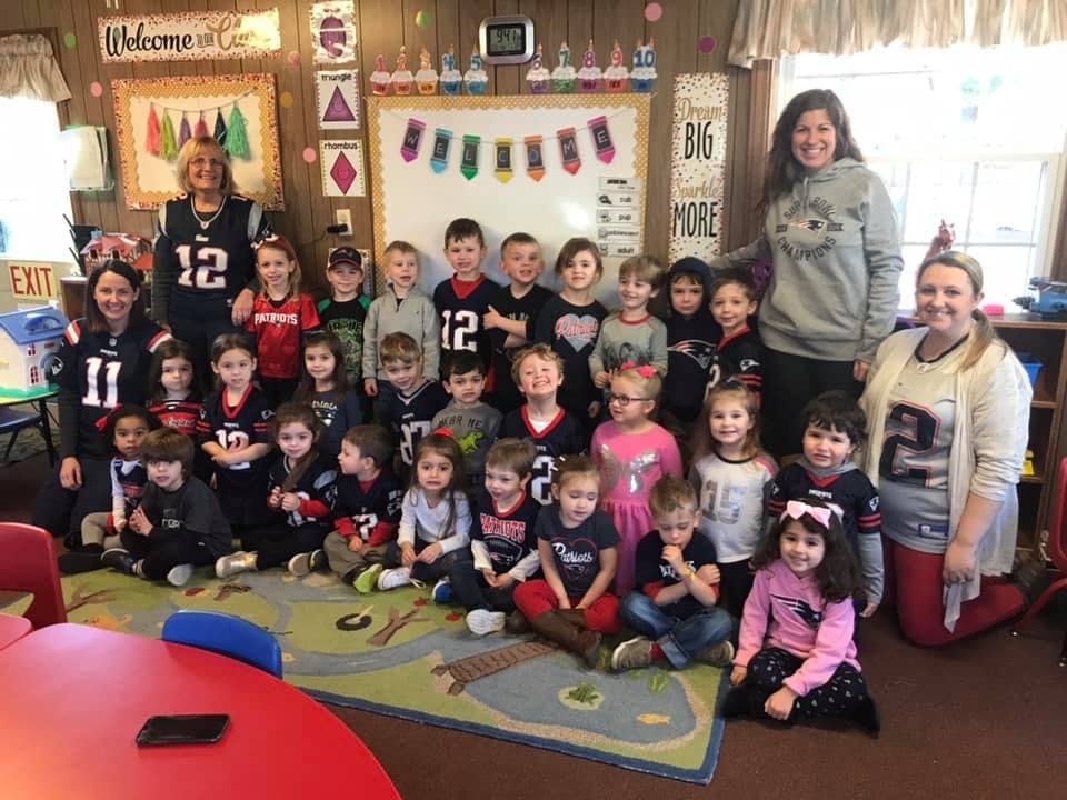 Two adults and a group of children posing for a photo in a classroom