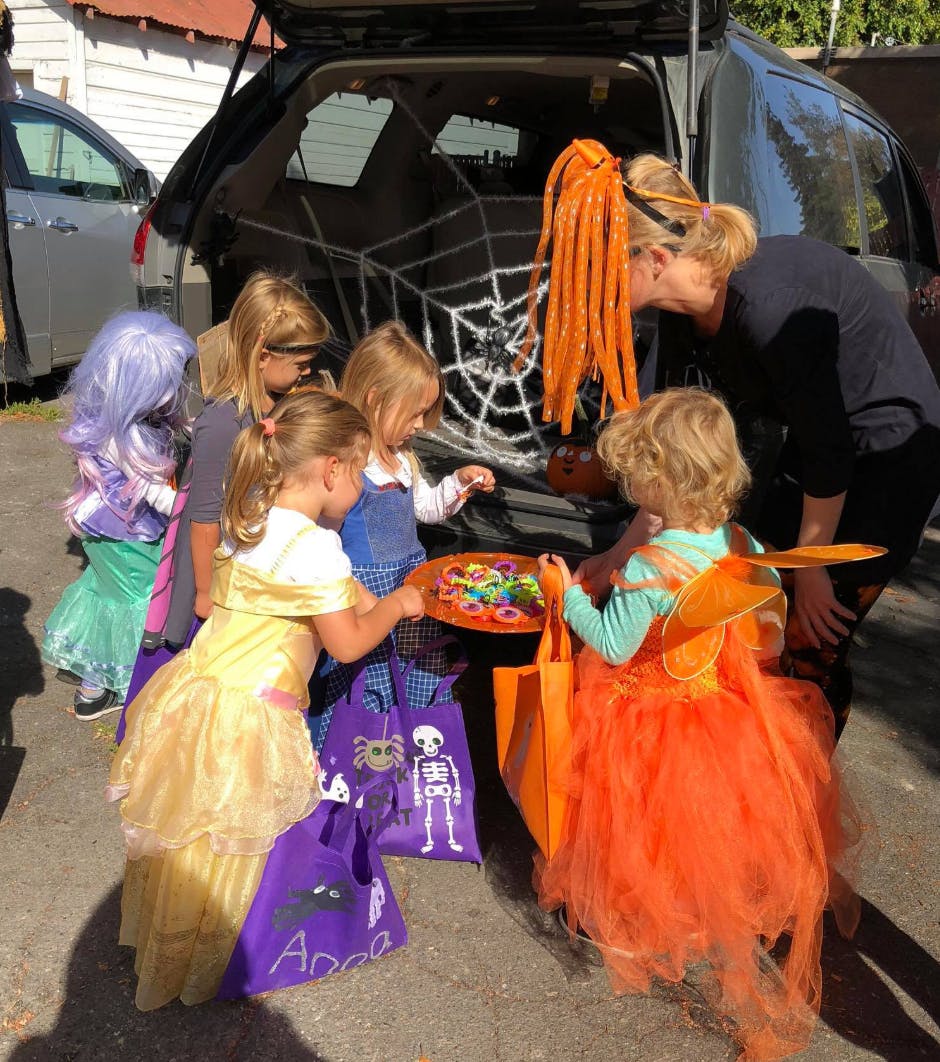 Adult and children in costumes getting candy from a car trunk