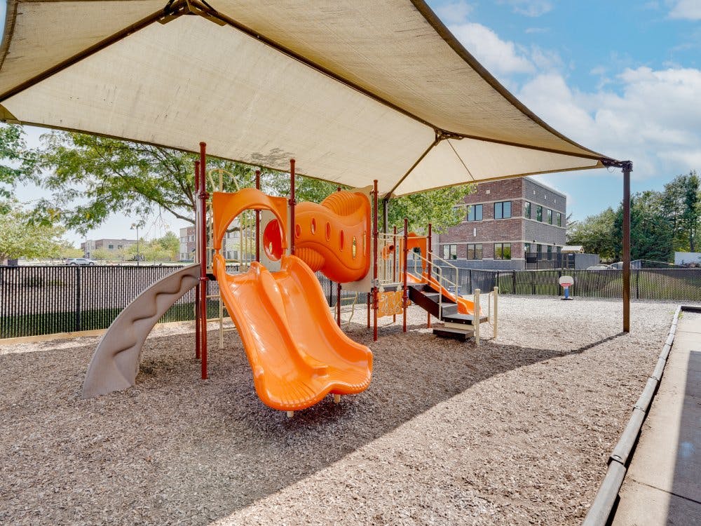 A playground with orange slides and a tan sunshade covering it