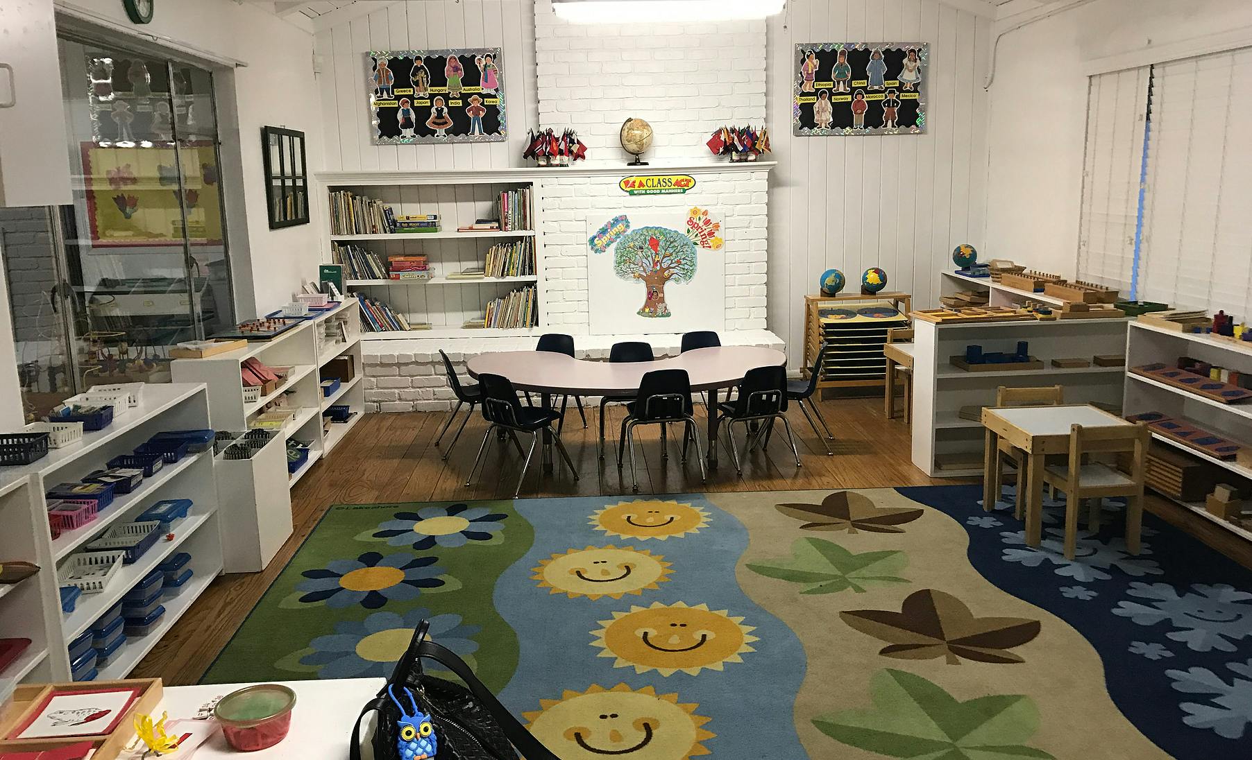 Classroom with tables, chairs, shelves, and a colorful rug