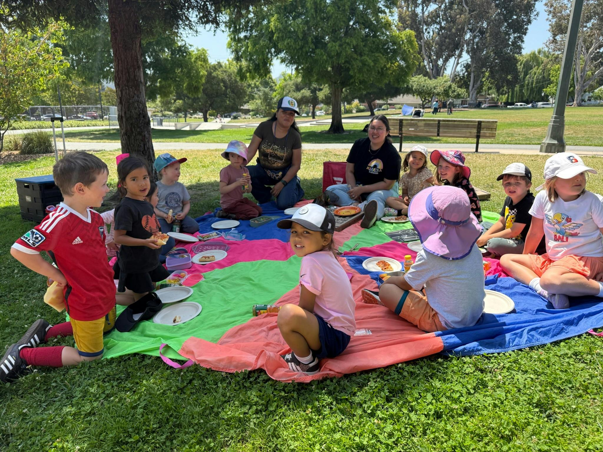 Adults and children sitting on blankets on grass, eating