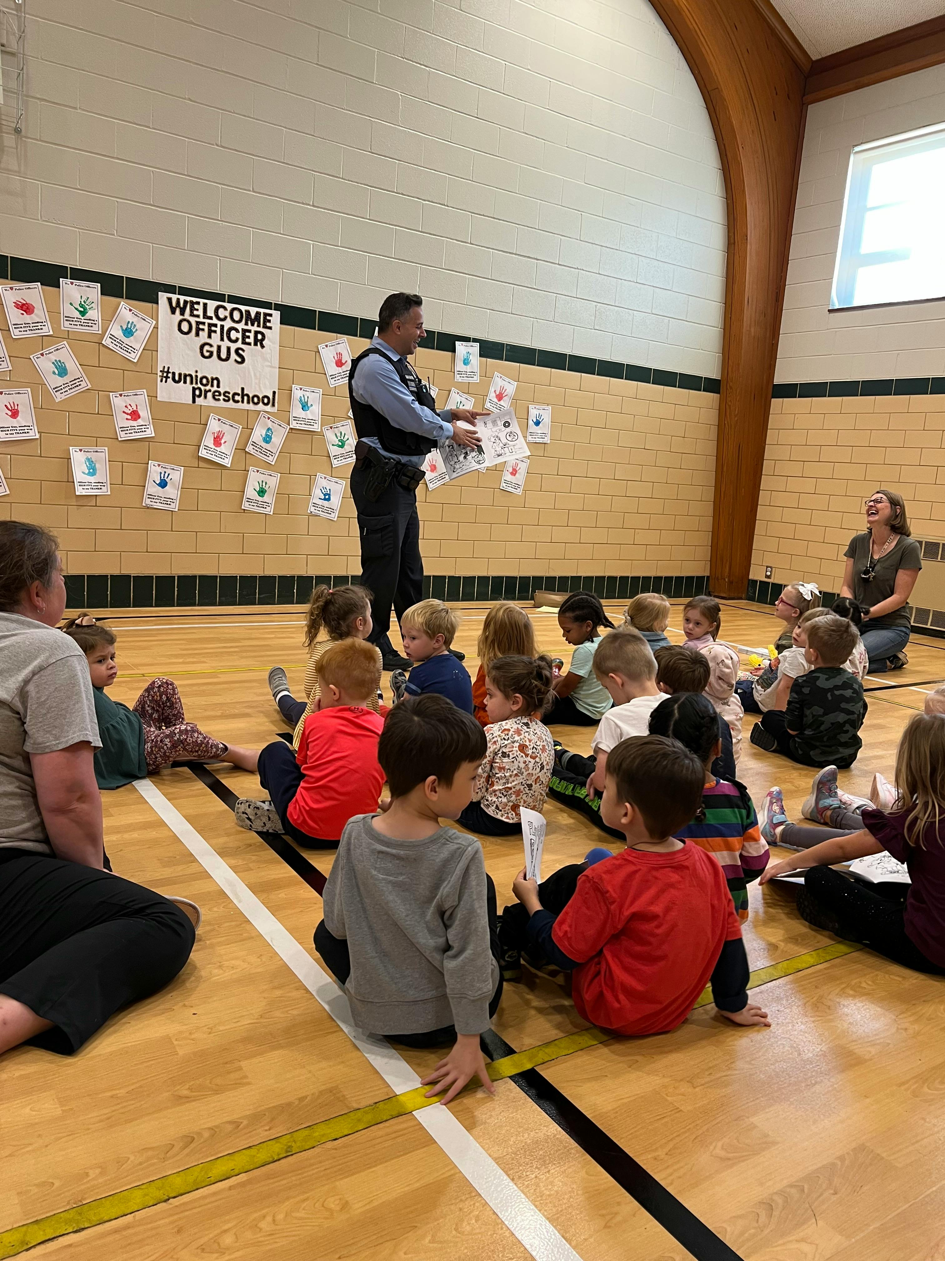 Adult in uniform speaking to a group of children sitting on a gym floor