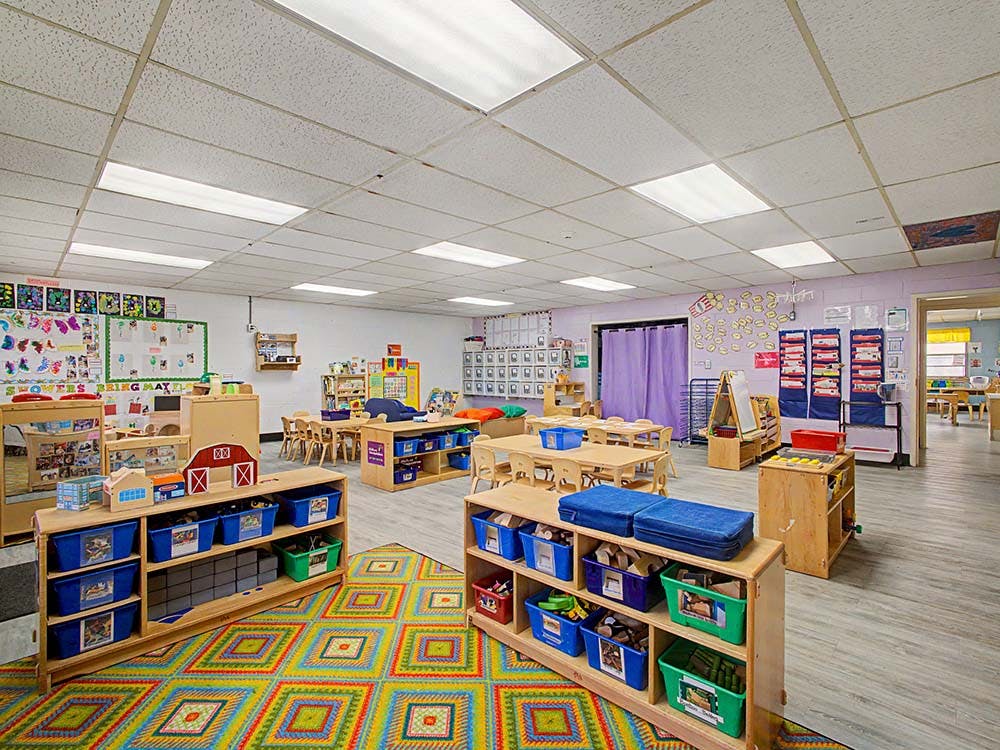 Classroom with colorful rug, small tables, chairs, and shelves