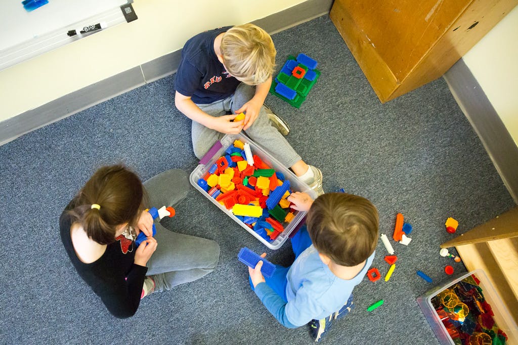 Three children playing with colorful building blocks on the floor