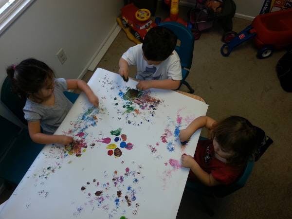 Three children finger painting on a large sheet of paper