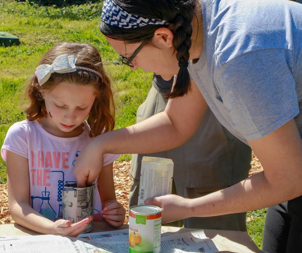 Person helping a child with a craft project outdoors