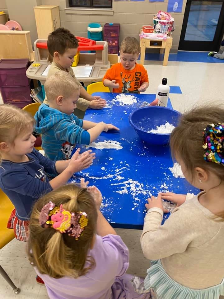 Children playing with white powder on a blue table